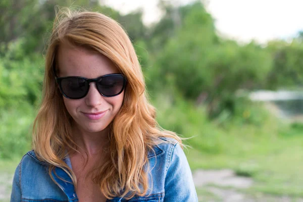 Uśmiechnięta kobieta w kapeluszu i okularach przeciwsłonecznych na plaży.